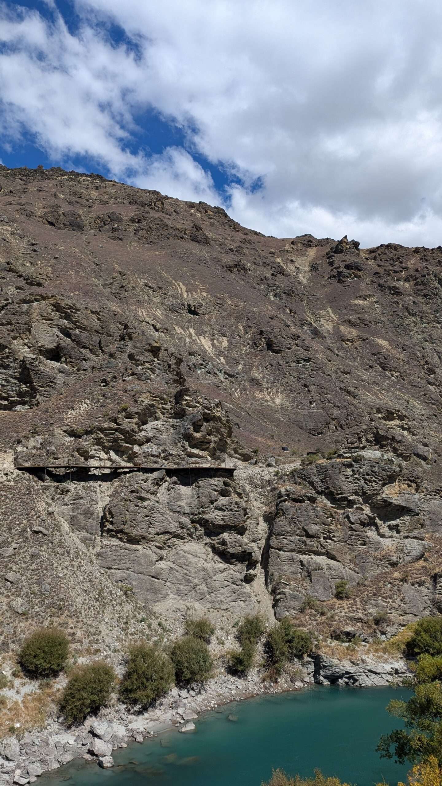 A cantilever bridge clings like a ribbon to the sheer rock face above the Kawarau River, hanging high above the gorge, suspended between design and daring.