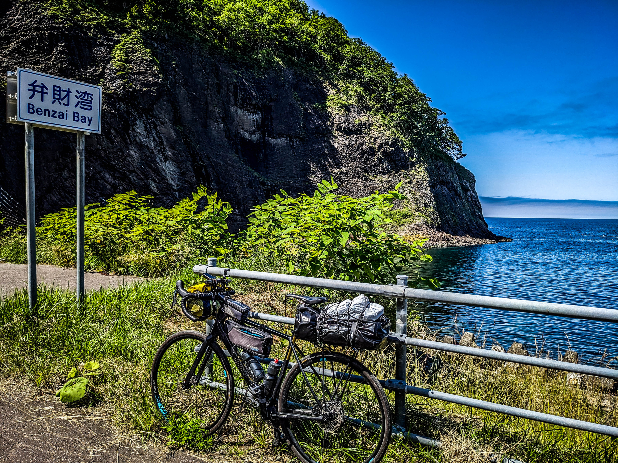 Fully-loaded touring bicycle leans against railing at rocky shorline of Benzai Bay, Hokkaido.