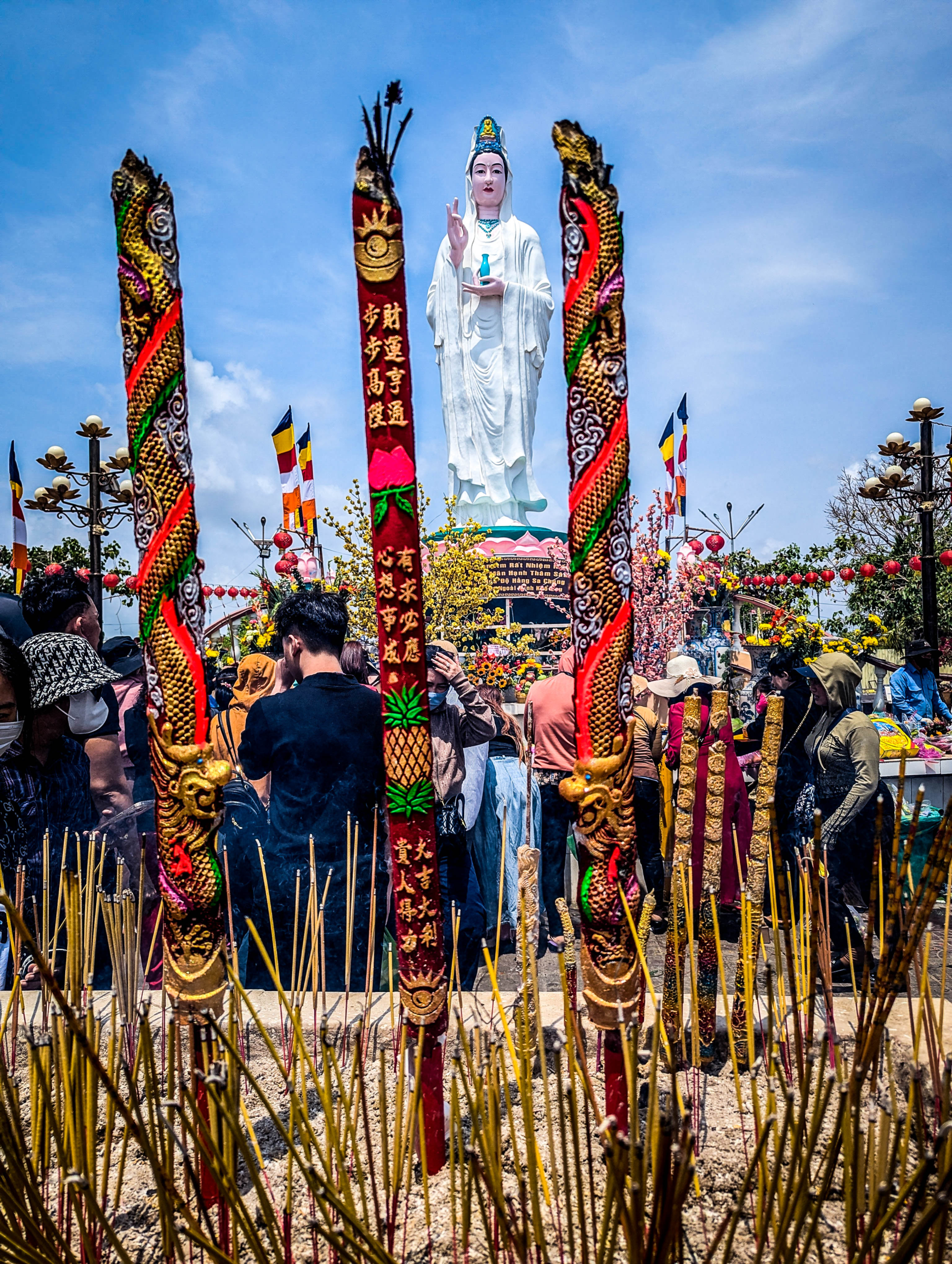 Quan Âm Phật Đài — The Goddess of Mercy in the background; elaborate burning sticks of incense in the foreground; in between worshippers stand praying.